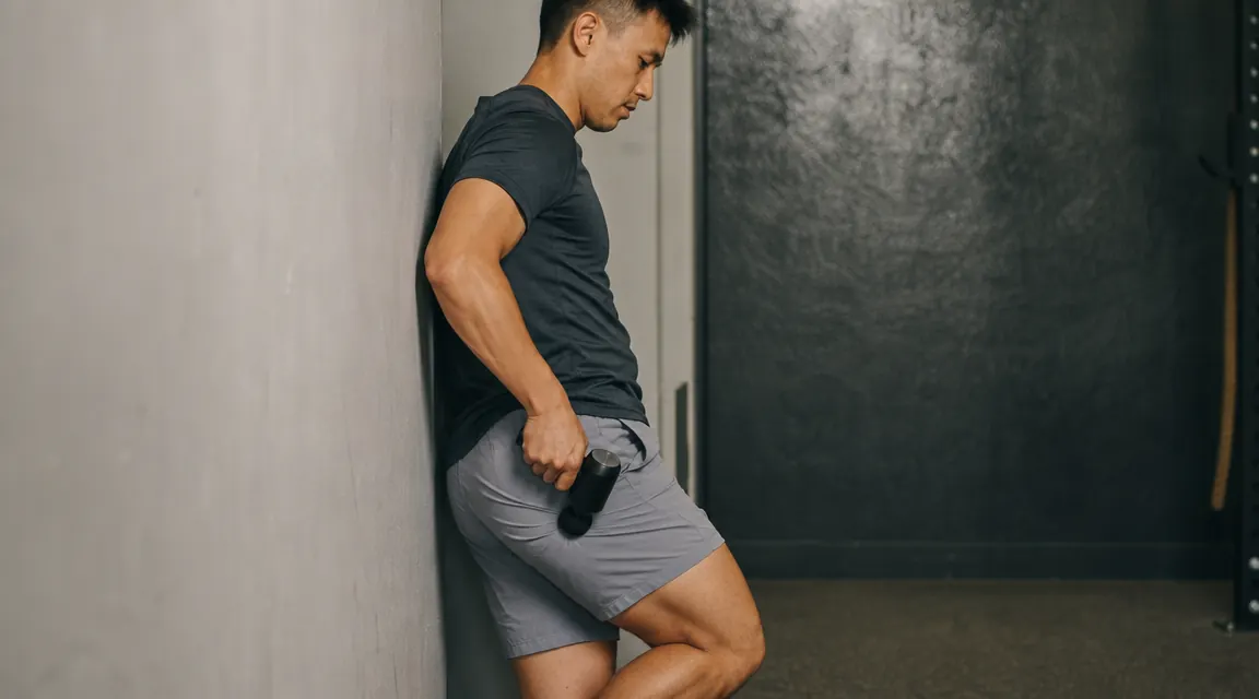 Person pressing a mini massage gun against a dense glute muscle while leaning into a wall for additional pressure