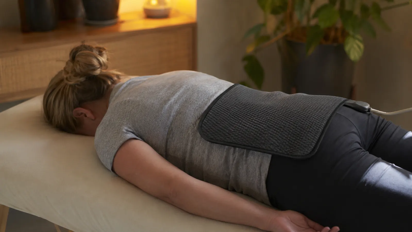Person lying face-down on a massage table with a heating pad on their mid-back, relaxed post-workout pose
